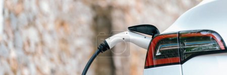 Photo for Panorama closeup EV charger handle plugged in or connect to electric car, recharging EV car battery with alternative and sustainable energy with zero CO2 emission for clean environment. Perpetual - Royalty Free Image