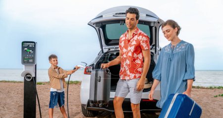 Photo for Family vacation trip traveling by the beach with electric car, lovely family taking luggage out while charging EV car battery with clean energy. Alternative family travel by eco-friendly car.Perpetual - Royalty Free Image