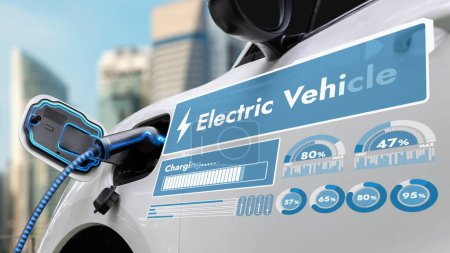 Foto de Enchufe eléctrico del coche con la estación de carga para recargar la pantalla de la batería holograma inteligente del estado de la batería digital por el cable del cargador del EV en el fondo del paisaje urbano. Futura sostenibilidad energética innovadora. - Imagen libre de derechos