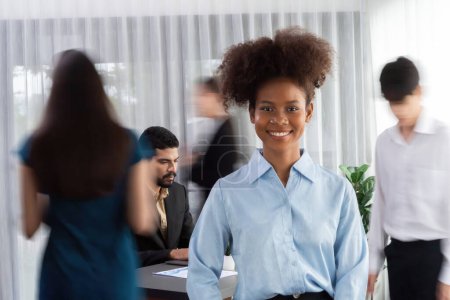 Téléchargez les photos : Jeune portrait de femme d'affaires africaine pose en toute confiance avec divers collègues dans la salle de réunion occupée en mouvement fond flou. Une équipe multiculturelle travaille ensemble à la réussite de l'entreprise. Concord - en image libre de droit