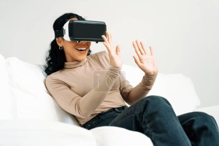 Foto de Mujer joven que usa gafas VR de realidad virtual en casa para una experiencia de compra en línea crucial. La innovación de realidad virtual VR optimizada para el estilo de vida de entretenimiento digital femenino. - Imagen libre de derechos
