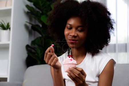 Photo for Portrait of beautiful young African blogger tasting piece of cherry cake in concept special cuisine. Presenting cute cupcake decorate fruit for content creating on social media. Tastemaker. - Royalty Free Image