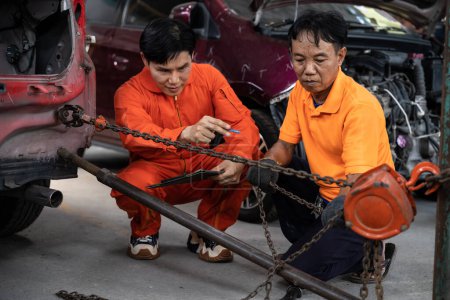 Photo for Mechanic testing strength and reliability of chain hoist for car towing in car workshop garage. Automotive service worker ensure through inspection of mechanical equipment. Oxus - Royalty Free Image