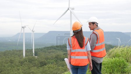 Photo for Male and female engineers working on a wind farm atop a hill or mountain in the rural. Progressive ideal for the future production of renewable, sustainable energy. - Royalty Free Image