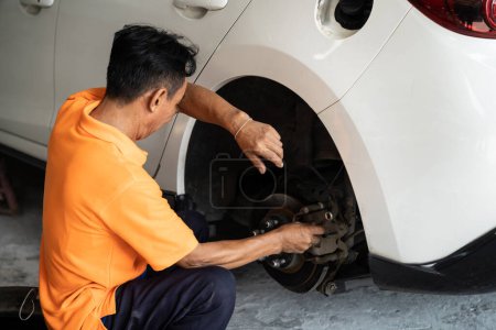 Photo for Hardworking mechanic changing car wheel in auto repair workshop. Automotive service worker changing leaking rubber tire in concept of professional car care and maintenance. Oxus - Royalty Free Image
