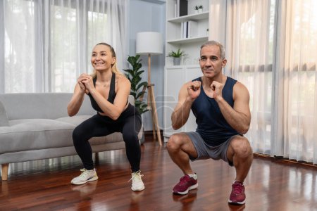 Photo for Athletic and sporty senior couple engaging in leg day training session with squat together at home exercise as concept of healthy fit body lifestyle after retirement. Clout - Royalty Free Image