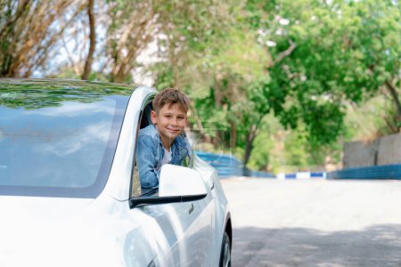 Téléchargez les photos : Petit garçon excité et heureux avec le sourire sur le visage apparaissent sur la fenêtre de la voiture tout en conduisant, expression ludique et joyeuse pendant le voyage en voiture pendant l'été. Perpétuel - en image libre de droit