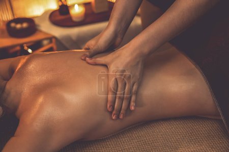Téléchargez les photos : Grosse cliente profitant d'un massage relaxant anti-stress spa et dorloter avec la beauté de la peau loisirs dans la bougie chaude éclairage salon de spa ambiant à la station de luxe ou à l'hôtel. Tranquillité - en image libre de droit