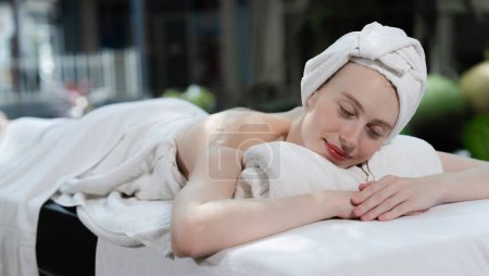 Téléchargez les photos : Belle jeune femme se détend sur un lit de spa entouré par la nature. prêt pour un massage du corps. Jolie femelle en serviette blanche couchée paisiblement pendant l'attente d'un massage du corps. Ferme là. Tranquillité - en image libre de droit
