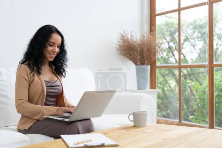 Téléchargez les photos : Femme afro-américaine utilisant un ordinateur portable pour un travail crucial sur Internet. Secrétaire ou rédaction de contenu en ligne travaillant à domicile. - en image libre de droit