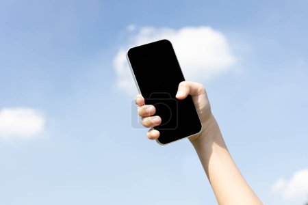 Téléchargez les photos : Smartphone recyclable tenu en main sur fond de ciel. Les déchets électroniques portatifs destinés au recyclage réduisent et réutilisent le concept pour promouvoir un environnement propre grâce à la gestion du recyclage. Pneumatique - en image libre de droit