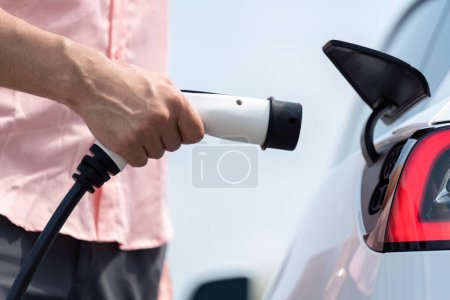 Téléchargez les photos : Branchez le chargeur EV à la main dans le véhicule électrique pour recharger la batterie de voiture EV de la station de charge extérieure. Environnement de jour frais avec concept alternatif d'énergie propre et durable. Perpétuel - en image libre de droit
