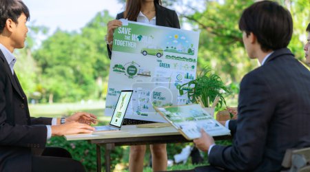 Foto de Grupo de empresarios asiáticos que presentan un plan de desarrollo respetuoso con el medio ambiente y un proyecto de tecnología sostenible para un futuro más ecológico, estableciendo una oficina de negocios ecológicos al aire libre en el parque natural.Gyre - Imagen libre de derechos