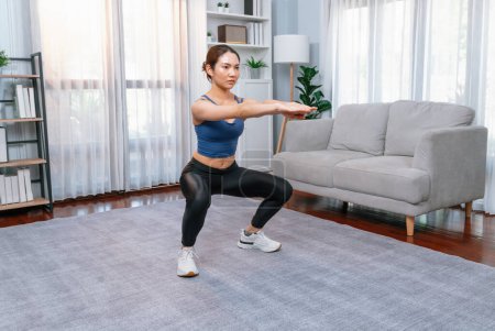 Photo for Vigorous energetic woman doing exercise at home. Young athletic asian woman strength and endurance training session as home workout routine with squat. - Royalty Free Image