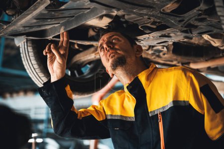 Photo for Vehicle mechanic conduct car inspection from beneath lifted vehicle. Automotive service technician in uniform carefully diagnosing and checking cars axles and undercarriage components. Oxus - Royalty Free Image