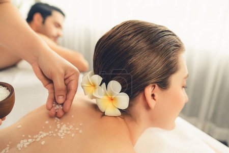 Photo for Blissful couple customer having exfoliation treatment in luxury spa salon with warmth candle light ambient. Salt scrub beauty treatment in health spa body scrub. Quiescent - Royalty Free Image