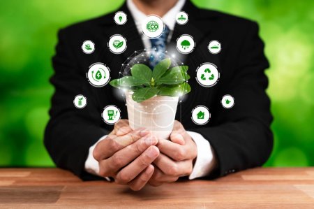 Foto de El empresario que sostiene una planta verde con un icono de diseño digital ecológico simboliza un negocio respetuoso con el medio ambiente con el compromiso de ESG de reducir las emisiones de carbono mediante el uso de energía limpia y sostenible. Dependencia - Imagen libre de derechos