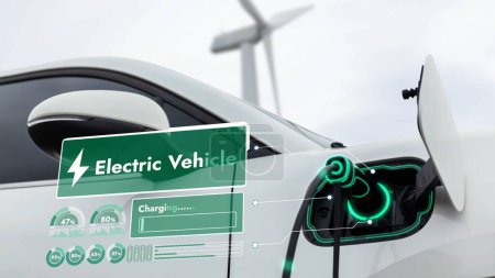Téléchargez les photos : L'énergie de recharge de voiture électrique de la station de charge EV affiche l'hologramme futuriste d'état de batterie intelligente par le câble de prise de chargeur EV dans le parc d'éoliennes. Durabilité des énergies propres alternatives. Pertinence - en image libre de droit