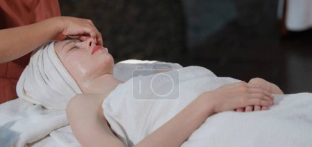 Foto de Una hermosa mujer caucásica joven teniendo masaje facial mientras se encuentra en la cama de spa rodeado de equipos de belleza eléctrica. Máscara facial de belleza. Rodeado de equipo médico en el salón de spa. Tranquilidad. - Imagen libre de derechos