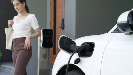 Photo for A woman unplugs the electric vehicles charger at his residence. Concept of the use of electric vehicles in a progressive lifestyle contributes to a clean and healthy environment. - Royalty Free Image