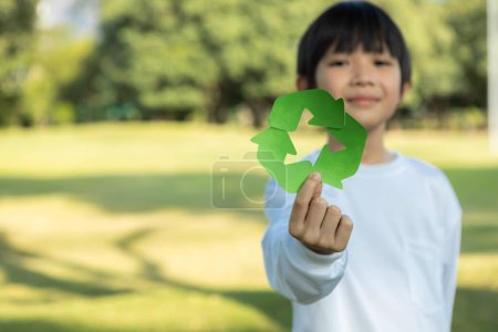 Fröhlicher junger asiatischer Junge, der das Recycling-Symbol auf dem natürlichen grünen Tageslicht-Park hält und das Recycling, die Reduzierung und Wiederverwendung von Abfällen fördert, um zukünftigen Generationen ein ökologisch nachhaltiges Bewusstsein zu vermitteln. Kreisel