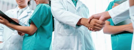 Photo for Group of medical staff doctor nurse and healthcare specialist profession handshaking in hospital. Medical teamwork and healthcare cooperation in panoramic banner background. Neoteric - Royalty Free Image