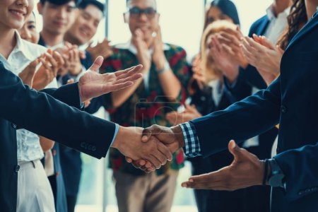 Photo for Cropped image of businessmen shaking hand and making a contract in the sign of agreement, cooperation rounded with smiling employees clapping hands and applause behind. Front view. Intellectual. - Royalty Free Image