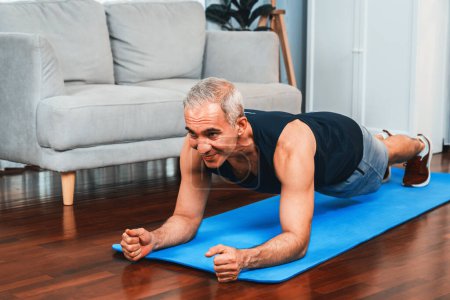 Foto de Hombre mayor atlético y deportivo planking en la alfombra de ejercicio de fitness en el ejercicio en casa como concepto de estilo de vida corporal en forma saludable después de la jubilación. Clout. - Imagen libre de derechos