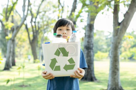 Foto de Alegre joven asiático niño sosteniendo papelera símbolo de reciclaje en el parque natural verde luz del día promover el reciclaje de residuos, reducir, y reutilizar el estímulo para la conciencia eco sostenible para la generación futura. Gyre. - Imagen libre de derechos