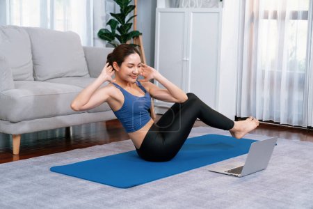 Photo for Asian woman in sportswear doing crunch on exercising mat as home workout training routine. Attractive girl engage in her pursuit of healthy lifestyle with online exercise training video. Vigorous - Royalty Free Image