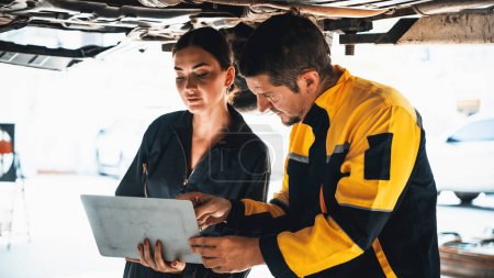 Photo for Two vehicle mechanic working together underneath lifted car, conduct car inspection with laptop. Automotive service technician in uniform carefully make diagnostic troubleshooting. Panorama Oxus - Royalty Free Image