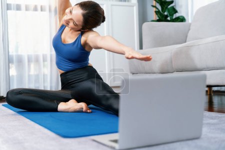 Foto de Computadora portátil enfocada en el suelo que muestra video de entrenamiento de ejercicio en línea, mientras que la mujer atlética deportiva se concentra en la rutina de calentamiento y estiramiento en un fondo borroso. Vigoroso - Imagen libre de derechos