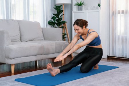 Téléchargez les photos : Femme asiatique en vêtements de sport faisant de l'exercice de yoga sur tapis de fitness comme sa routine d'entraînement à domicile. Soins du corps sains et méditation calme dans le style de vie de yoga avec confortable et détente. Vigoureux - en image libre de droit