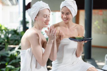 Photo for Portrait of two attractive woman in towel giggling during hold the herbal bowl surrounded by natural spa environment. Pretty girls with beautiful skin using herbal scrub at spa salon.Tranquility. - Royalty Free Image