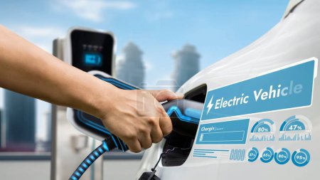 Photo for Hand insert EV charger and recharge electric car from charging station displaying futuristic battery status hologram on blur background of cityscape. Smart sustainable clean energy. Peruse - Royalty Free Image