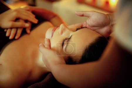 Photo for Closeup caucasian woman enjoying relaxing anti-stress head massage and pampering facial beauty skin recreation leisure in warm candle lighting ambient salon spa in luxury resort or hotel. Quiescent - Royalty Free Image