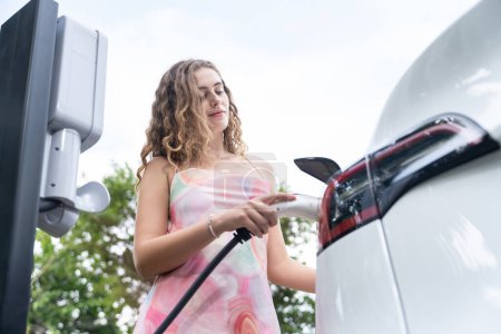 Photo for Eco-friendly conscious woman recharging modern electric vehicle from EV charging station. EV car technology utilized as alternative transportation for future sustainability. Synchronos - Royalty Free Image