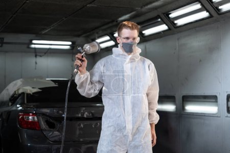 Photo for Automotive service worker in protective gear expertly applying color paint in to cars bodywork with spray gun or respirator painting in chamber workshop. Car paint service for scratch refinish. Oxus - Royalty Free Image