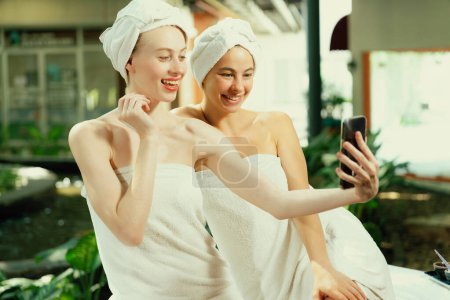 Téléchargez les photos : Couple de jeunes belles femmes avec une belle peau en serviette blanche prenant une photo ensemble à l'extérieur entouré d'un environnement naturel paisible. Beauté et concept de spa sain. Tranquillité. - en image libre de droit