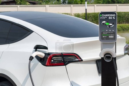Téléchargez les photos : Batterie de recharge de voiture électrique EV au parking dans le parc vert de la ville. Technologie d'énergie propre alternative pour une automobile rechargeable pour des déplacements urbains durables et respectueux de l'environnement. Expedient - en image libre de droit