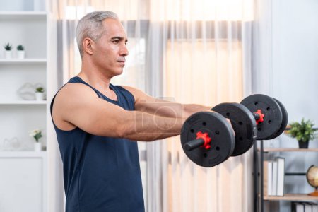 Photo for Athletic and sporty senior man engaging in body workout routine with lifting dumbbell at home as concept of healthy fit body with body weight lifestyle after retirement. Clout - Royalty Free Image