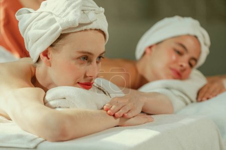 Téléchargez les photos : Un couple de belle jeune femme avec serviette blanche se trouvent sur un lit spa confortable pendant recevoir massage du corps relaxant par masseur professionnel entouré au salon de spa. Fond gris. Tranquillité. - en image libre de droit