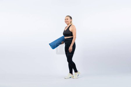 Photo for Full body length shot athletic and sporty senior woman holding fitness exercising mat on isolated background. Healthy active physique and body care lifestyle after retirement. Clout - Royalty Free Image
