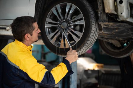 Photo for Hardworking mechanic changing car wheel under car lifting station. Automotive service worker changing leaking rubber tire in concept of professional car care and maintenance. Oxus - Royalty Free Image