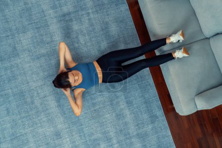 Foto de Top view joven atractiva mujer asiática en ropa deportiva se encuentra en el suelo y haciendo abdominales en el agacharse, ayudando a apuntar en el músculo abdominales para la rutina de ejercicio en casa eficaz. Vigoroso - Imagen libre de derechos