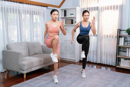 Foto de Mujer asiática atlética enérgica y fuerte con compañero de entrenamiento corriendo en su lugar en su casa. Búsqueda de físico en forma y compromiso con un estilo de vida saludable con entrenamiento en casa y entrenamiento. Vigoroso - Imagen libre de derechos