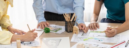 Photo for A portrait of professional architect team discussion about architectural project on meeting table with blueprint and wooden block scatter around at modern office. Closeup. Focus hand. Delineation. - Royalty Free Image