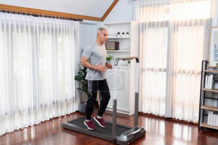 Photo for Active senior man running on tread running machine at home together in full body shot as fitness healthy lifestyle and body care after retirement for pensioner. Clout - Royalty Free Image