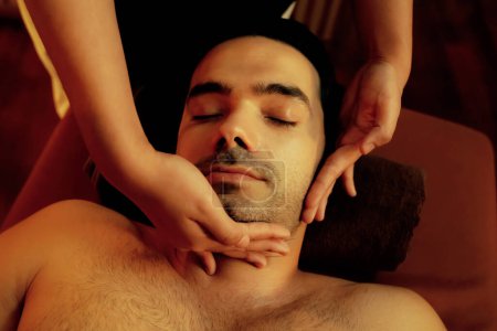 Photo for Caucasian man enjoying relaxing anti-stress head massage and pampering facial beauty skin recreation leisure in warm candle lighting ambient salon spa in luxury resort or hotel. Quiescent - Royalty Free Image