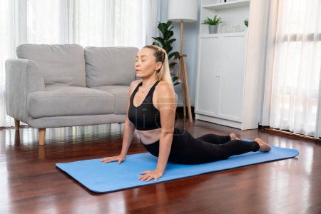 Photo for Senior woman in sportswear being doing yoga in meditation posture on exercising mat at home. Healthy senior pensioner lifestyle with peaceful mind and serenity. Clout - Royalty Free Image